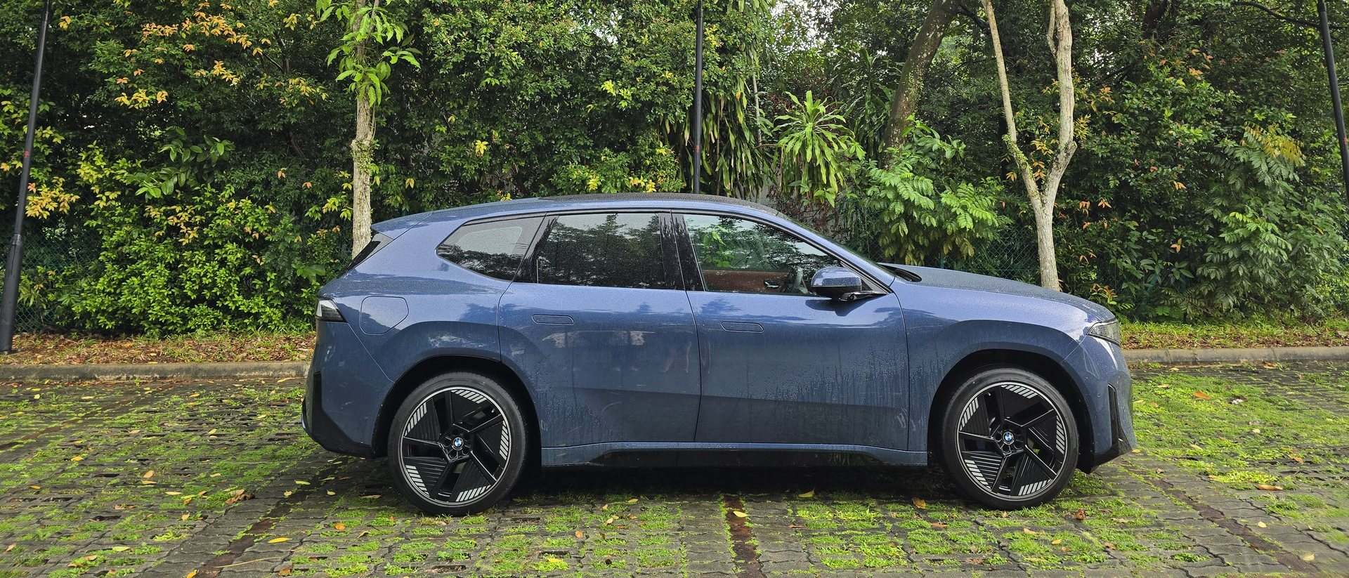 BMW iX3 in profile on a grass-brick carpark surrounded by tropical greenery in Singapore