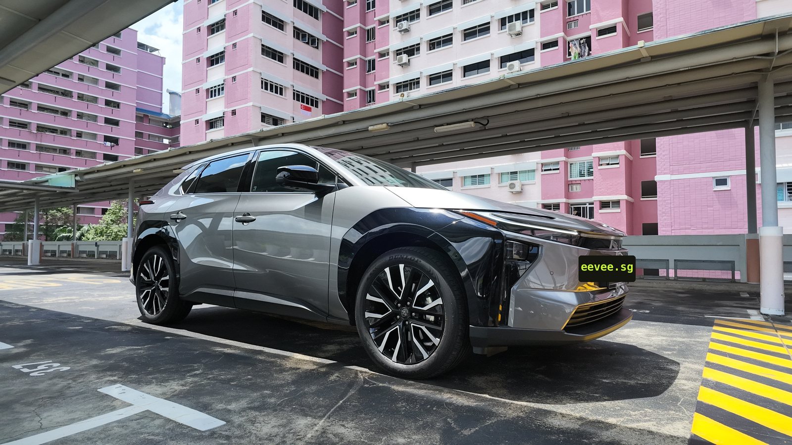 Toyota bZ4X front three-quarter view under a carpark shelter with pink HDB blocks behind it in Singapore