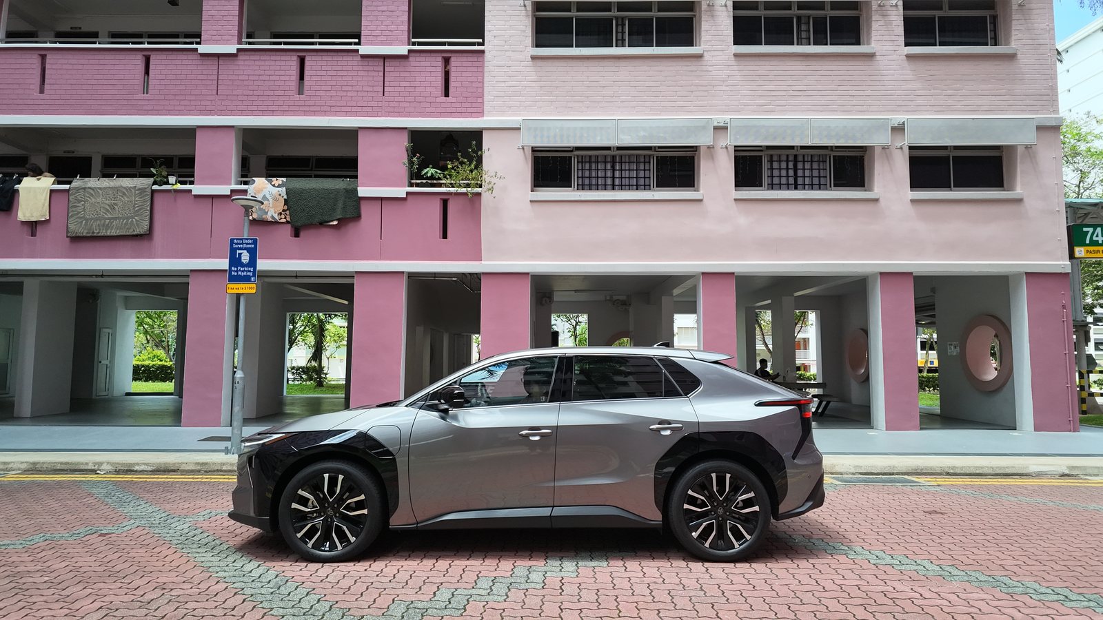 Toyota bZ4X in profile parked against a pink HDB block with laundry hanging from the racks