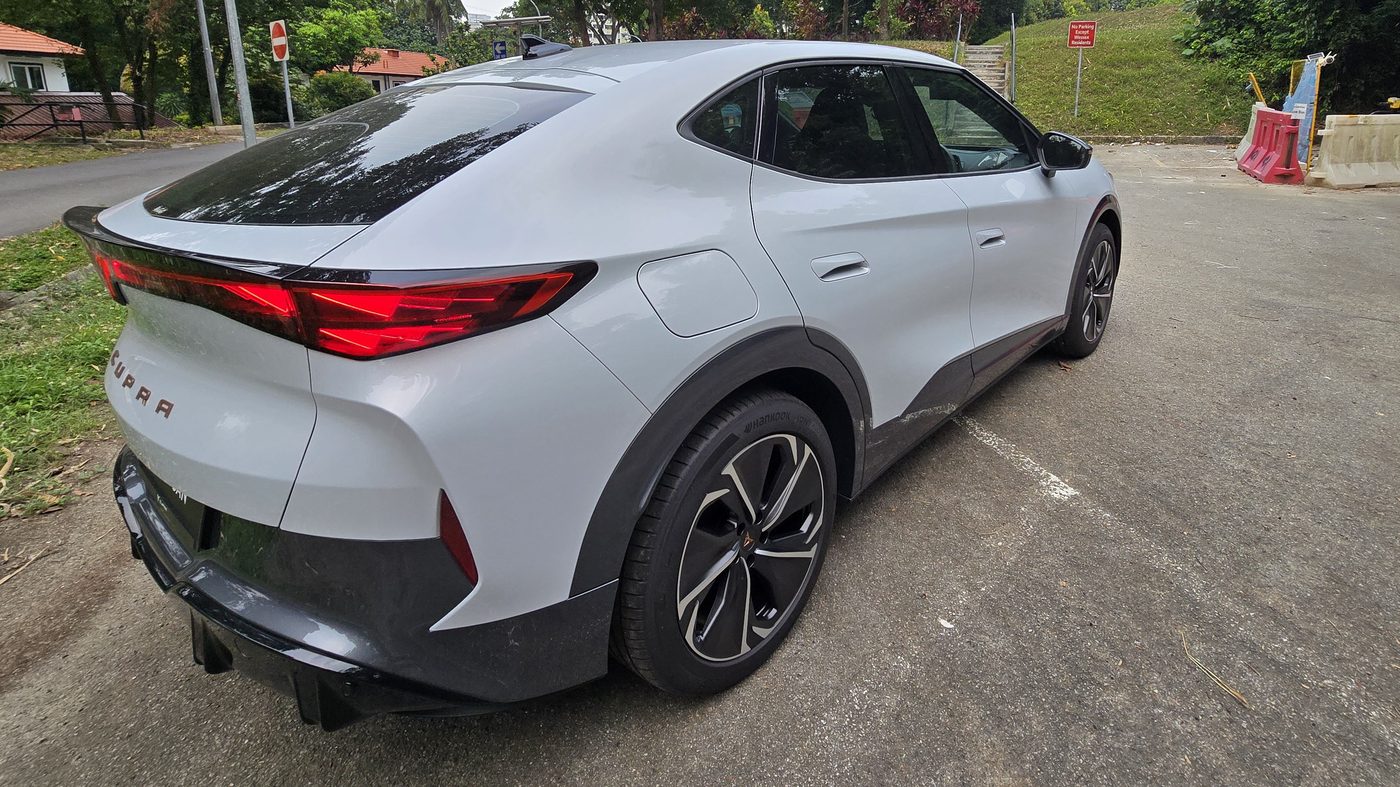 Cupra Tavascan rear three-quarter view showing the sloping roofline, the full-width light bar and the rear diffuser