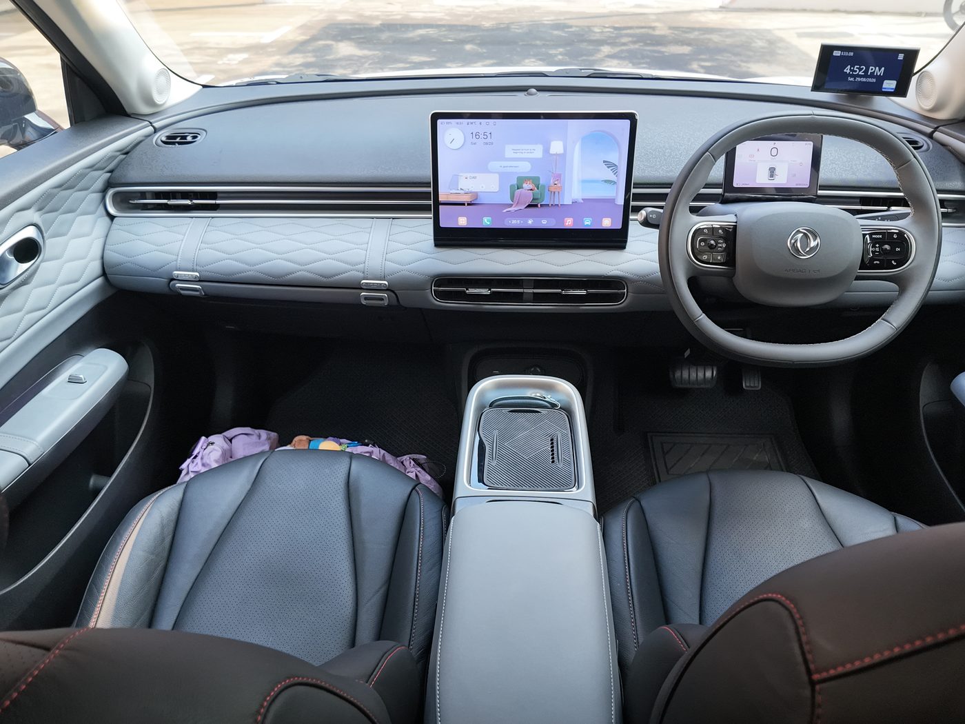 The Dongfeng Box R dashboard from the rear seat: quilted grey dash, 12.8-inch screen showing the interactive living room, and a makeup bag on the passenger seat