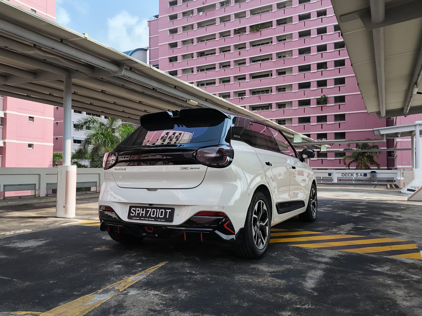 Rear three-quarter view of the Dongfeng Box R in Twilight White, showing the black spoiler and red-accented rear bumper, with pink HDB blocks behind