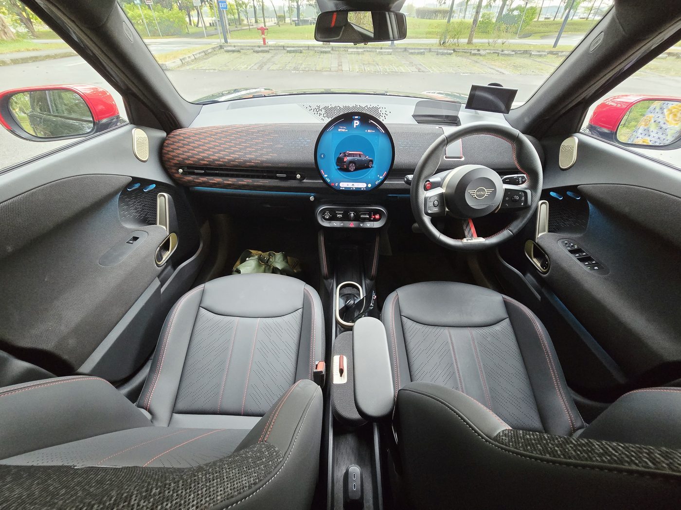The MINI JCW Aceman E cabin from the passenger side, showing the round OLED display, the toggle bar, the knitted fabric dash and the JCW sport seats