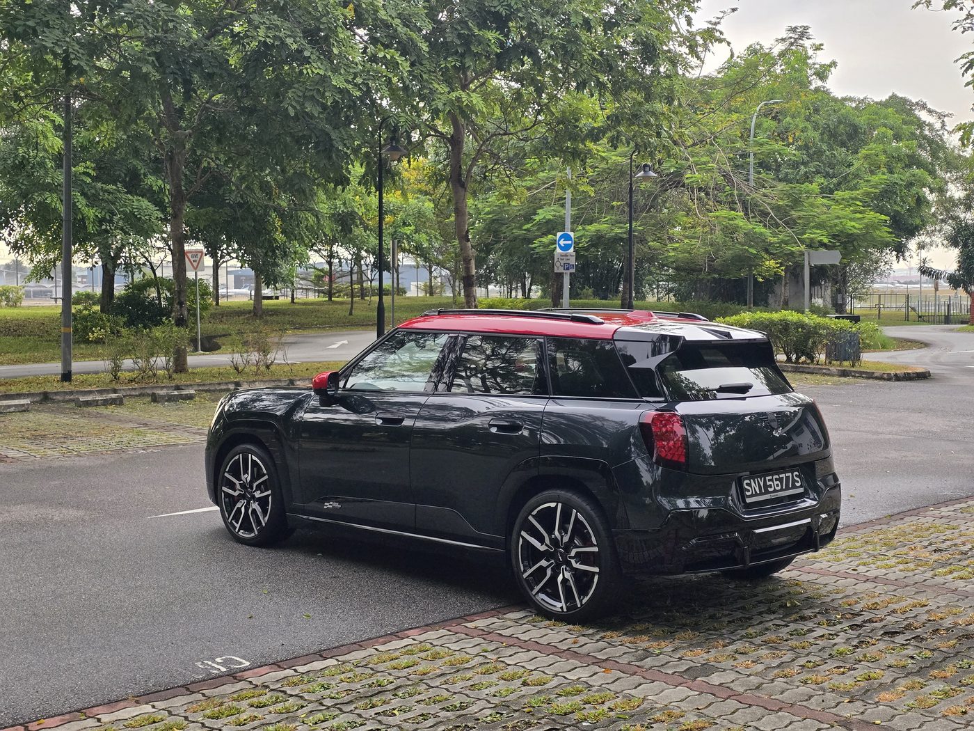 Rear three-quarter view of the MINI JCW Aceman E in British Racing Green with a red roof, parked on a quiet road in Singapore