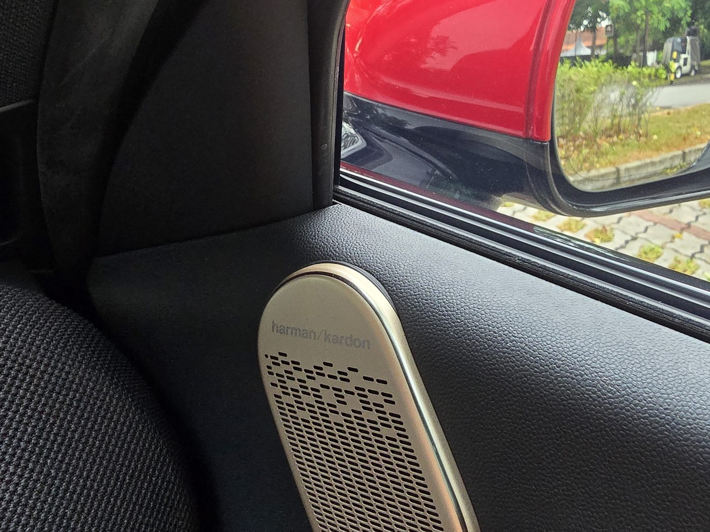 Gold-finished Harman Kardon tweeter on the MINI JCW Aceman E's door, with the red wing mirror behind it