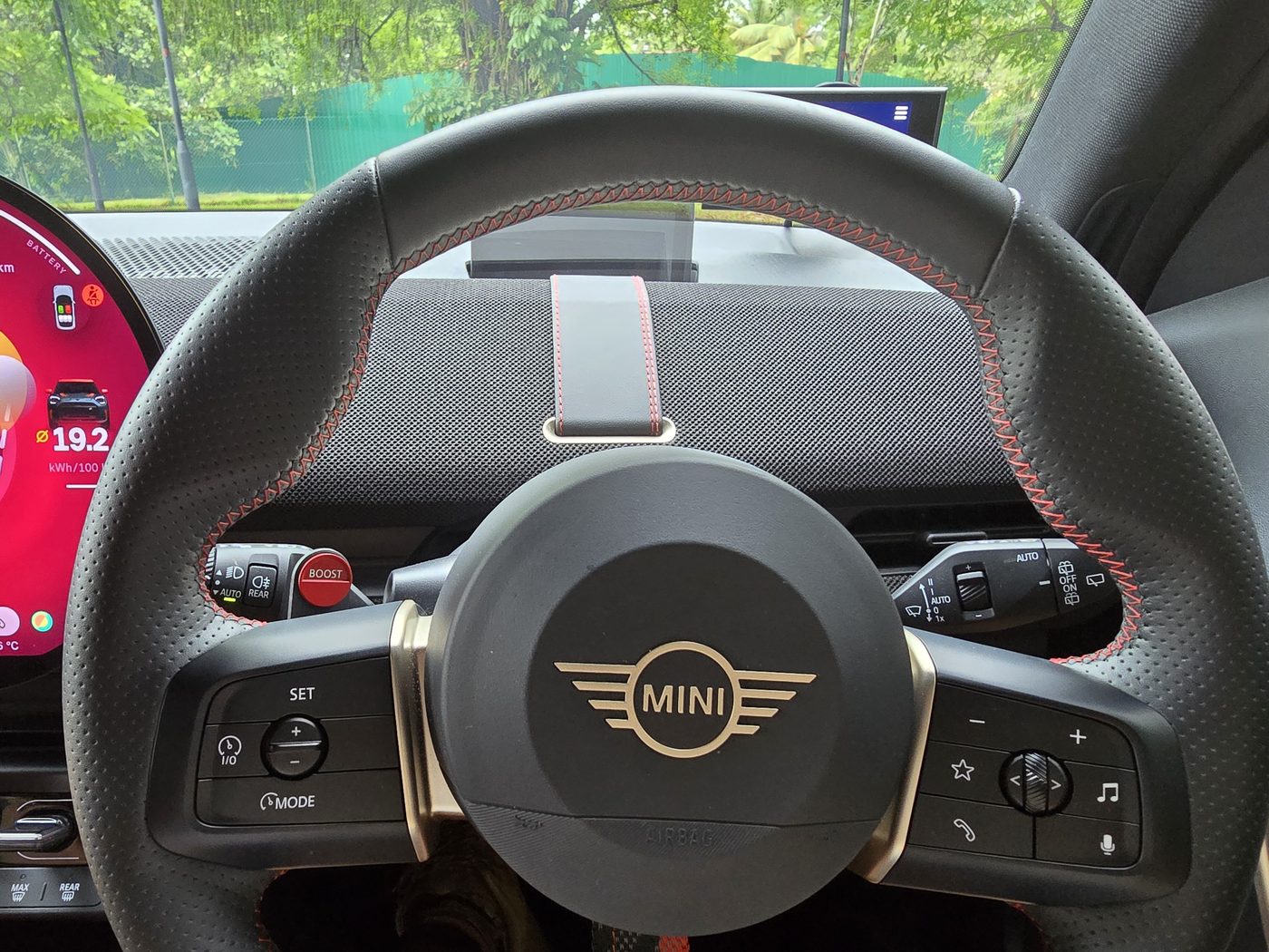 The MINI JCW Aceman E steering wheel with physical buttons and the boost paddle, viewed from the driver's seat
