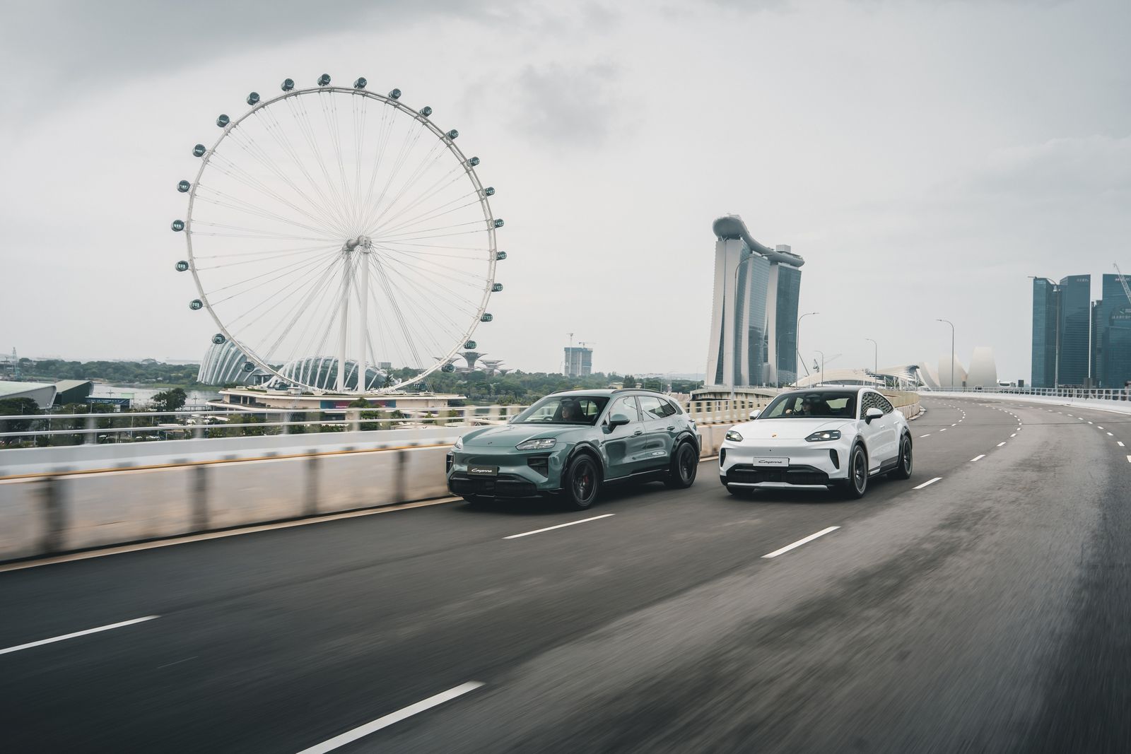 Porsche Cayenne Electric and Cayenne Coupé Electric driving past the Singapore Flyer and Marina Bay Sands