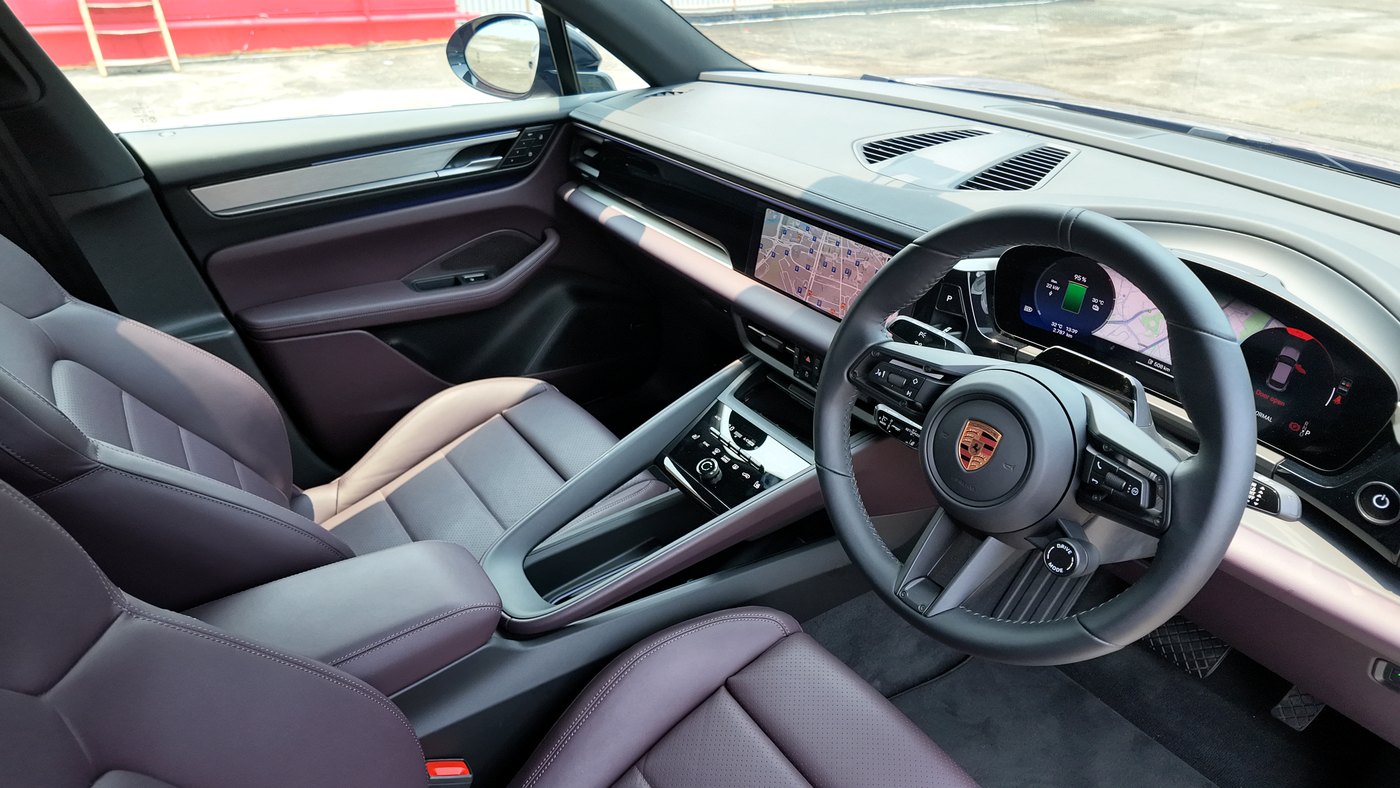 Porsche Macan Electric cabin in Bramble leather seen through the open driver's door, with the steering wheel, curved driver display, centre screen and console