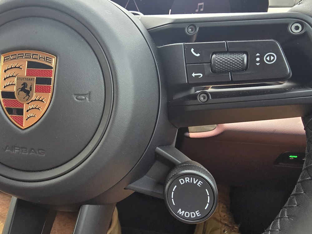 Knurled drive mode dial on the Porsche Macan Electric steering wheel, below the Porsche crest