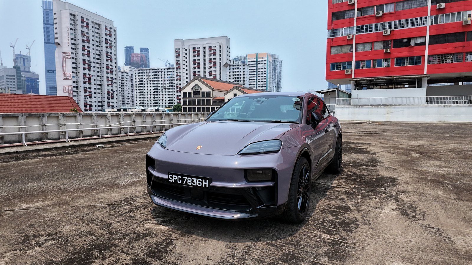 Provence purple Porsche Macan Electric, low front three-quarter view on a rooftop carpark with a red HDB block and the Singapore skyline behind it