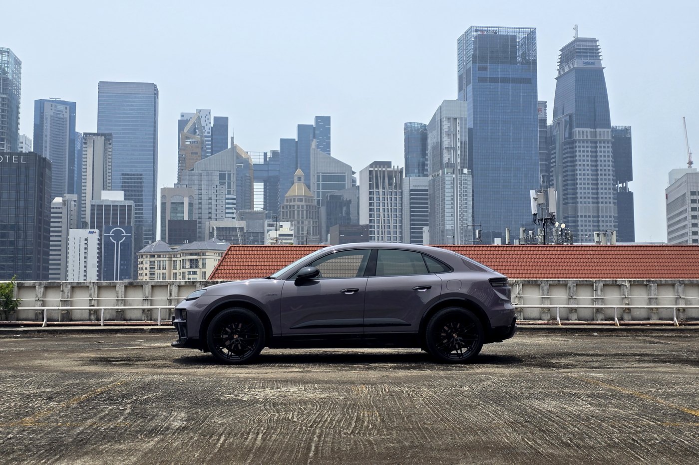 Porsche Macan Electric in profile on a rooftop carpark with the Singapore skyline behind it