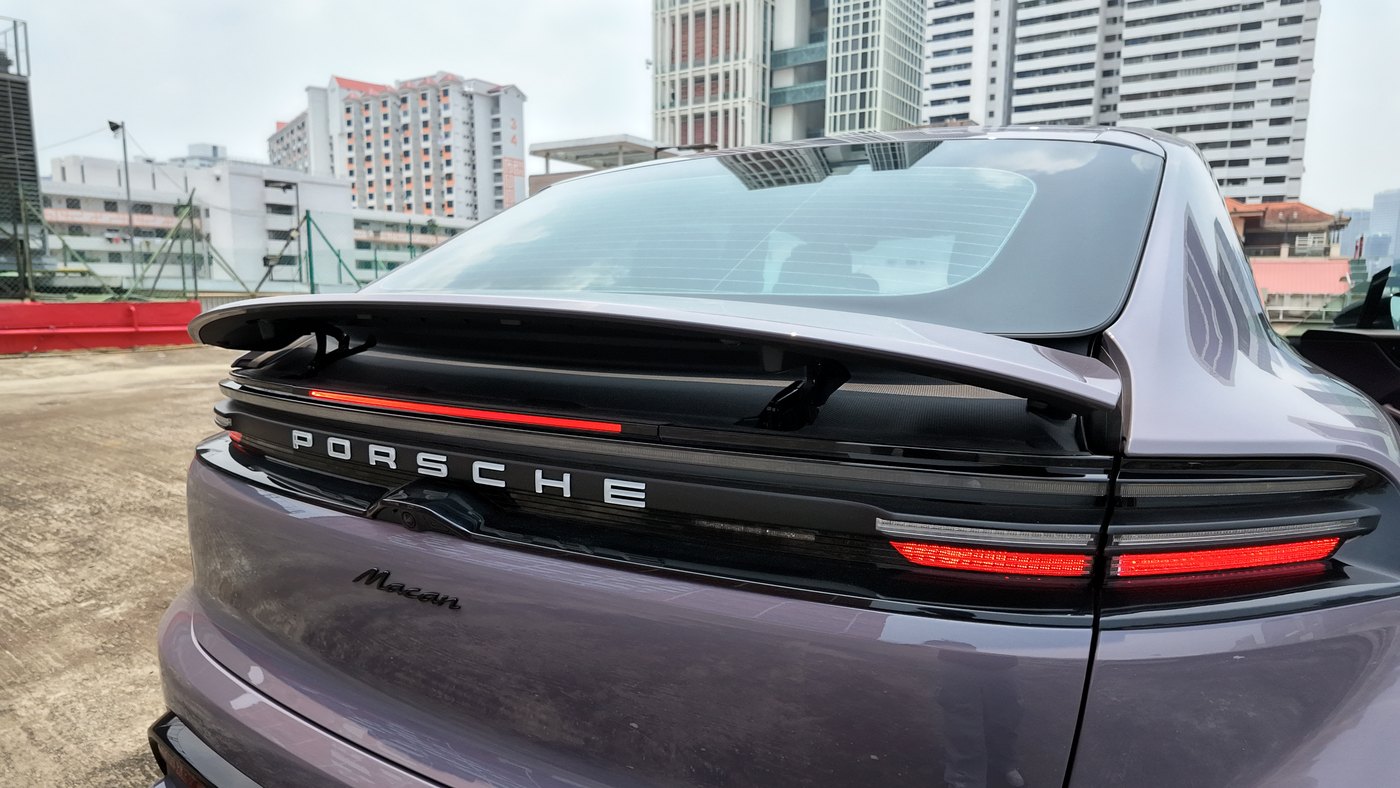 Rear of the Porsche Macan Electric with the adaptive spoiler raised above the full-width light bar and Porsche lettering