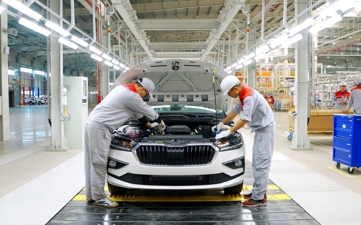 Two technicians working under the bonnet of a white Škoda on an assembly line