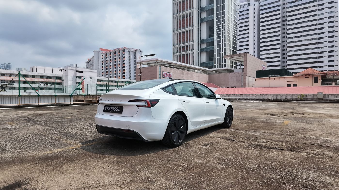 White Tesla Model 3 rear three-quarter view with Singapore flats behind
